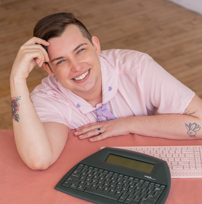 headshot of Aiden Feltkamp, a smiling white trans nonbinary person in a pink shirt with a black vest sitting on steps in new york city