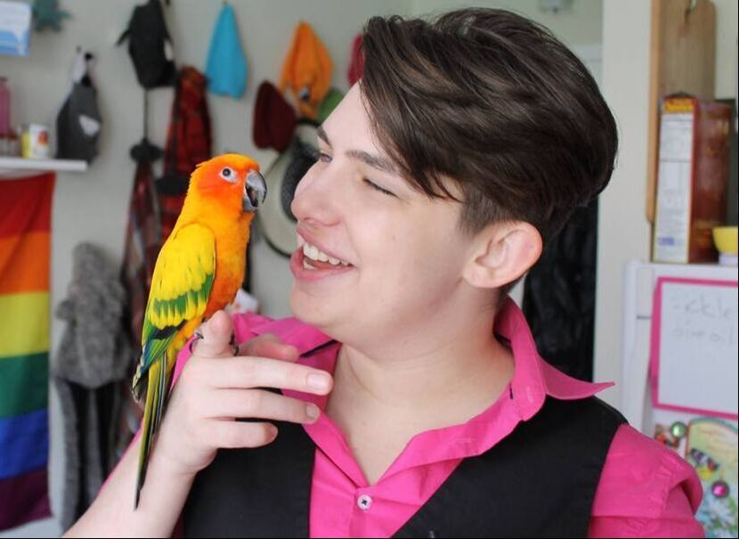 nonbinary person in pink shirt holding an orange parrot sun conure